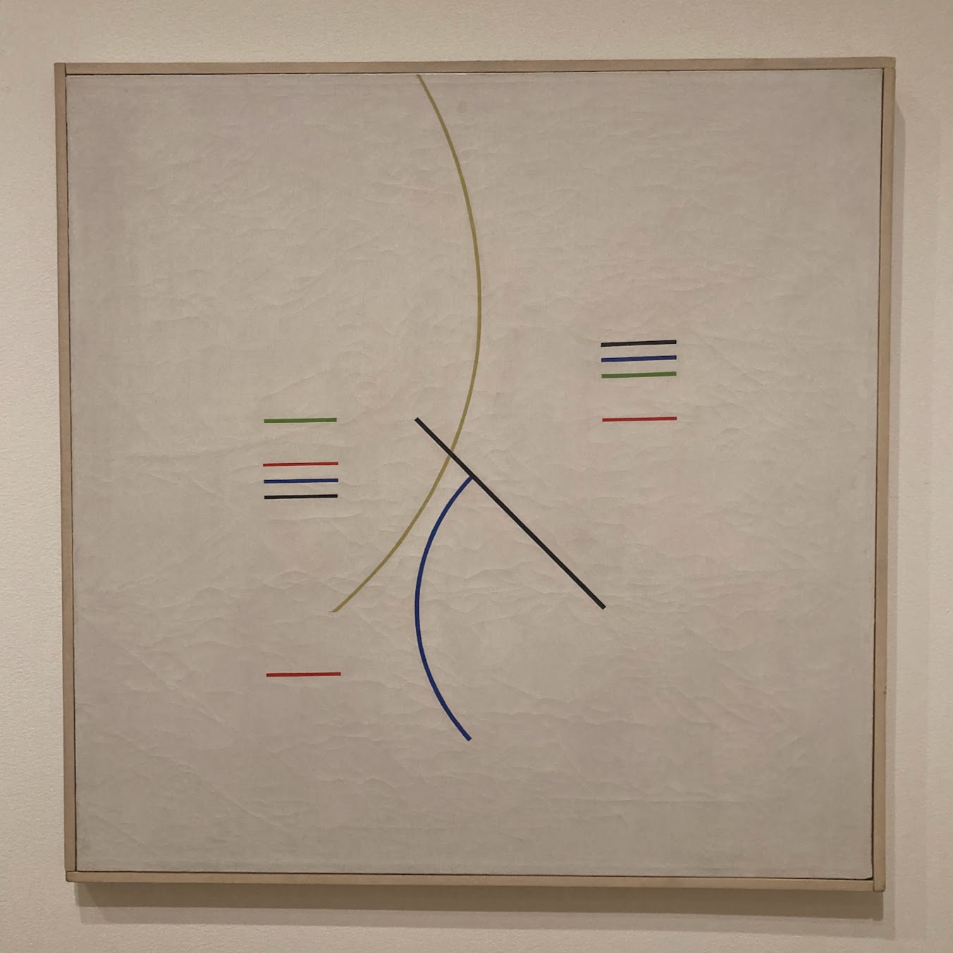 An oil painting of colorful geometric lines on a cream background. Starting at the top of the painting in the middle there is a dark yellow curve. Intersecting it in the center of the painting is a black line at a 45 degree angle and a dark blue curve. In the top right of the center area there are short horizontal black blue green and red lines. In the top left of the center area are horizontal green red blue and black lines. In the bottom left of the center there is a short horizontal red line. To us, the placement of these lines conveys a sense of balance and free movement. This in the spirit of Hlito's placement in art history, as one who rejected figurativism  and celebrated abstraction and geometry.